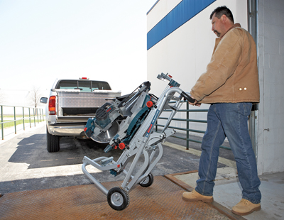 Man wearing a brown jacket and jeans pushing a Bosch saw on wheels towards a truck.