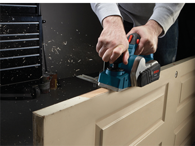 Person using a Bosch planer on a door. The tool is removing wood shavings.