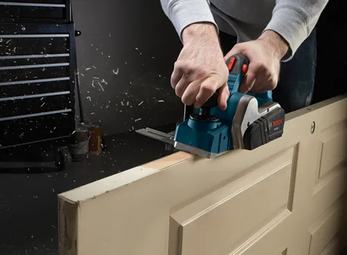 Bosch PL1632 power planer being used on a door, with wood shavings visible.
