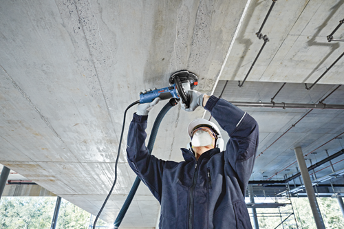 Person wearing safety gear using a Bosch CSG 15 concrete grinder on a concrete ceiling.