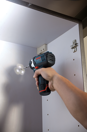 Bosch LITHIUM-ION impact drill being used to drill into a white cabinet.