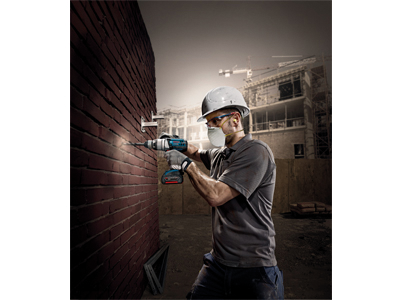 Person wearing safety gear drilling into a brick wall with a power tool.