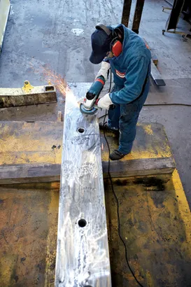 Person wearing protective gear grinds metal with an angle grinder, creating sparks.