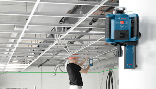 Bosch GCL 2-15 Professional laser on a wall, a person in a hard hat using a digital measuring device.