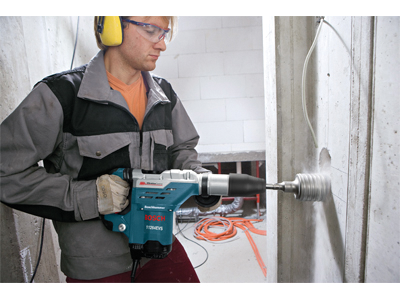 Person wearing protective eyewear and ear protection drilling into a concrete wall with a Bosch hammer, model 1125EVS.