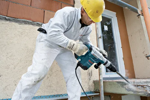 Person wearing protective gear uses a Bosch 11321EVS Boschhammer to work on a building.