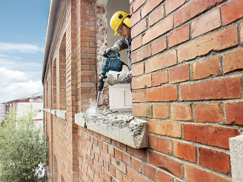 Man wearing safety gear using a Bosch 11321EVS demolition hammer to break concrete.