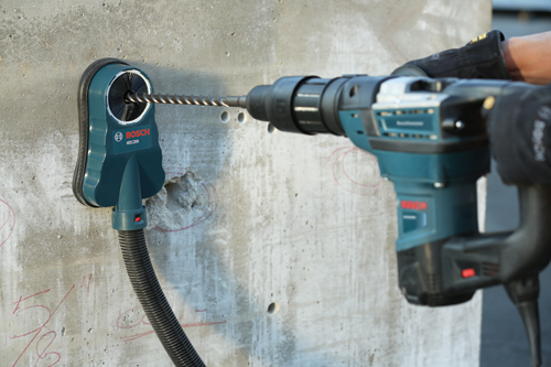 Bosch HDC200 dust extraction system attached to concrete, with Bosch hammer drill. A gloved hand holds the drill.
