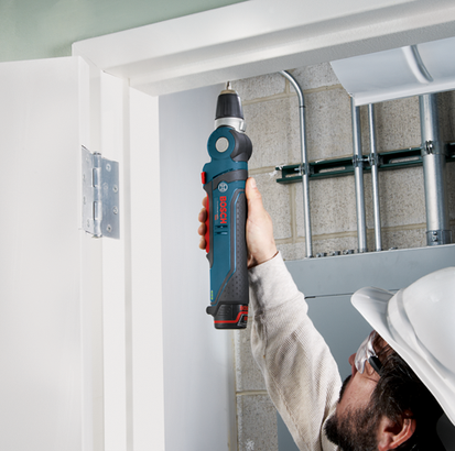 Bosch cordless drill being used by a person wearing a hard hat and safety glasses near a door hinge.
