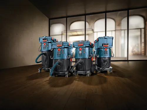 Four blue and black vacuums with red accents, on a hardwood floor, with windows and a blurred outdoor view in the background.