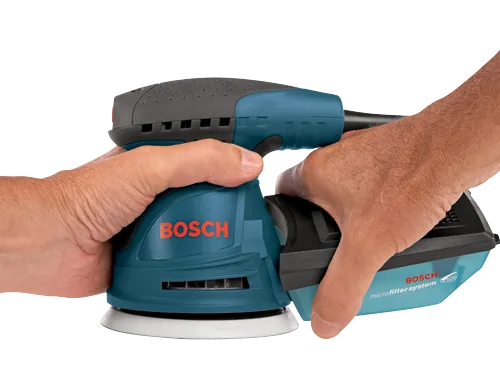 Hands holding a teal and black Bosch microfilter system sander with visible “BOSCH” branding.