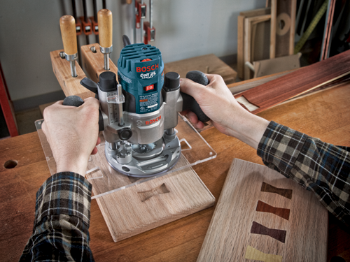 Bosch Colt 1.0 HP Palm Router PR20EVS being used on wooden projects. A person holds the router with both hands. There are two pieces of wood with bow tie shaped inlays.