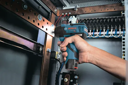 Bosch Lithium-Ion impact driver held by a person, EC motor, close to an electrical panel.