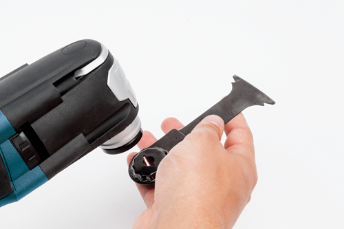 Hand holding an oscillating multi-tool blade; the power tool is in the background.