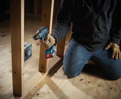 Bosch cordless drill being used to install an electrical box in a wooden frame.