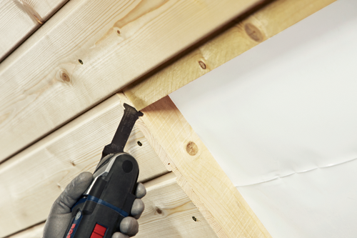 Bosch Aiz 32 Alb blade cutting wood, held by a gloved hand.