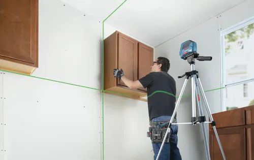 Man installing cabinets using a Bosch Professional line laser, with the BS 150 Professional tripod and green laser lines.