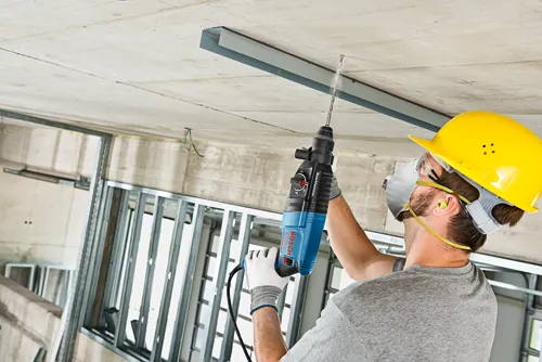 Person wearing safety gear drilling into ceiling with Bosch BULLDOG Xtreme hammer.