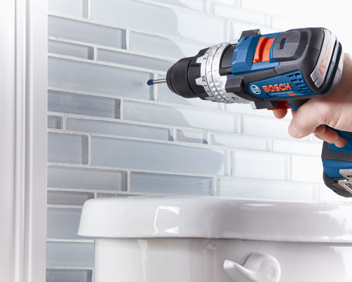 Bosch Lithium-Ion drill with EC brushless motor drilling into a tiled wall near a toilet.