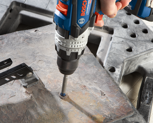 Bosch Lithium Ion drill is drilling into stone. The drill has "BOSCH" visible on it.