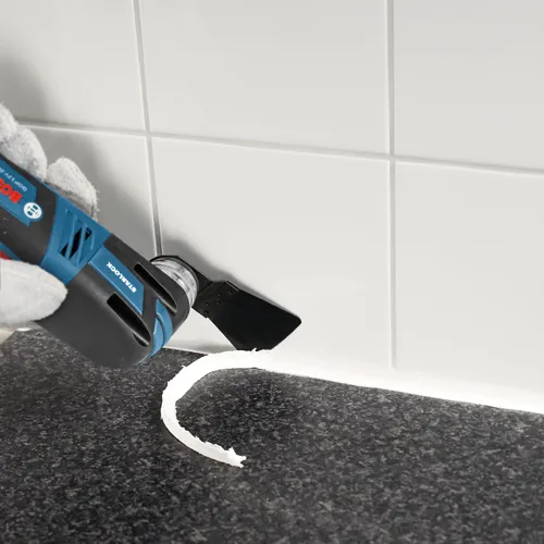 Bosch GOP 12V-28 tool with STARLOCK blade cutting white sealant from countertop edge.