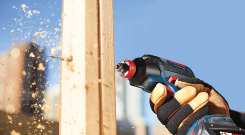 Bosch Lithium Ion impact driver drilling into wood with sawdust flying