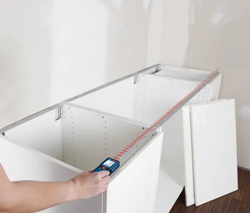 Bosch BLAZE laser measure, hand holding the measuring tool, on a cabinet, measures 4’1 ⅛” and 165’ 0”.