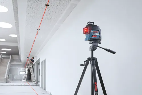 Bosch Professional GLI L3-300 level on a tripod projecting a red laser beam onto a ceiling, with a person on a ladder.