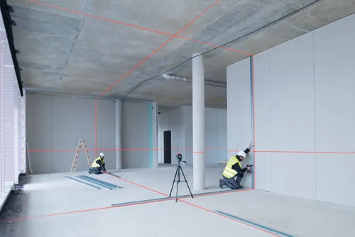 Construction workers in safety vests installing drywall, aided by red laser level lines.
