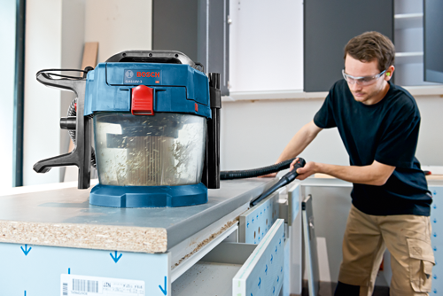 Bosch GAS18V-3 vacuum cleaner next to a person wearing safety glasses, cleaning a cabinet.