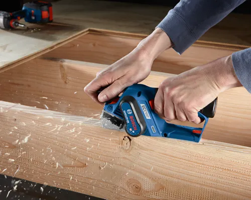 Bosch GHO12V-08 EC Brushless Motor planer is in use, shavings flying off the wood.