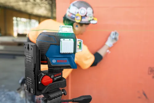 Bosch Professional GCL 2-15, emitting green laser lines, being used by a person wearing a hard hat and gloves.