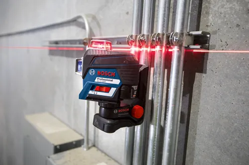 Bosch Professional GLL3-330C level projecting a red laser line on metal pipes with GUIDE-LINE and INCH-MARK markings.