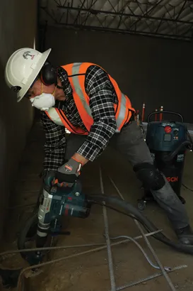 Person wearing protective gear operating a Bosch 11264EVS Boschhammer, vacuum positioned nearby.