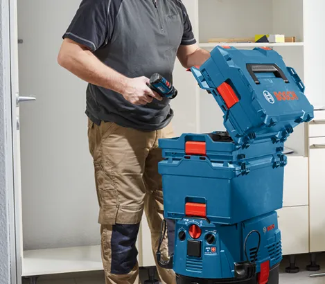 A person holding a drill, with the Bosch logo on a stackable blue box.