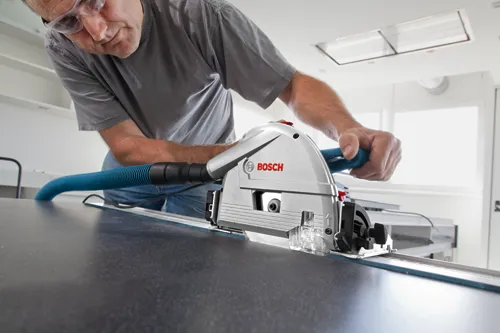 A person wearing safety glasses uses a Bosch saw to cut a surface.