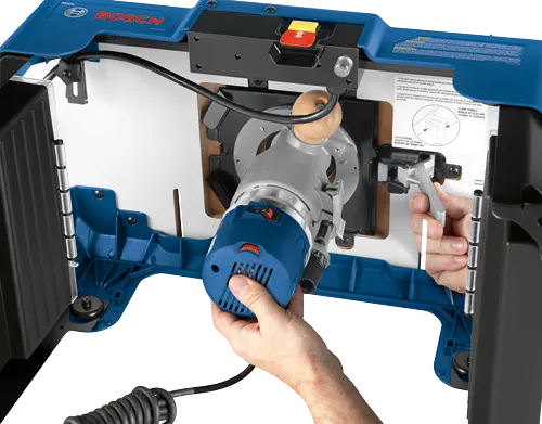 Bosch router mounted to a frame, with hands of a person holding it and an orange button visible. LATCH SPRING, RESORTE DE LA TRABA, RESSORT DE FERMETURE text is visible.