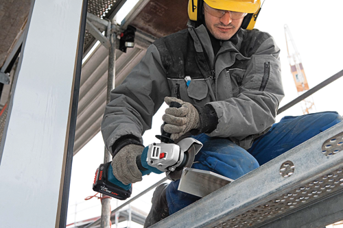 A person wearing protective gear using a Bosch CORE18V angle grinder.