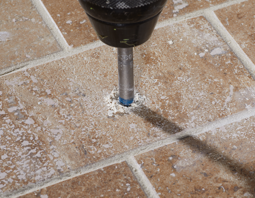 Drill bit drilling into tile, creating a hole.