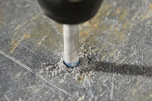 A drill bit is drilling into a stone surface, creating dust.