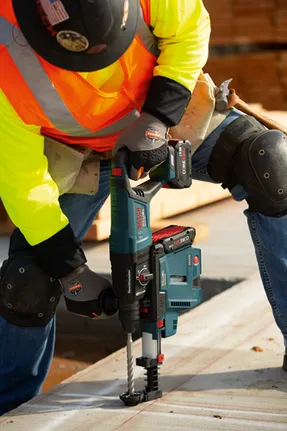 Construction worker using a Bosch GBH18V-26D Bulldog Boschhammer. The drill is powered by a CORE18V 8.0 Ah battery. The worker wears safety gear.