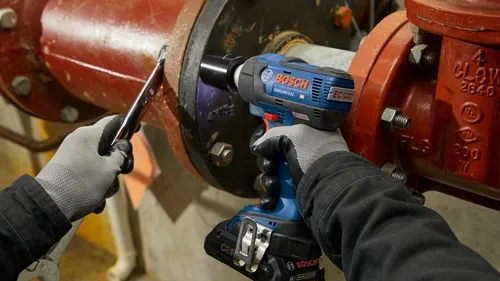 A person using a Bosch GDS18V-221 impact wrench and a wrench to work on a red pipe fixture; the wrench says "14/16".