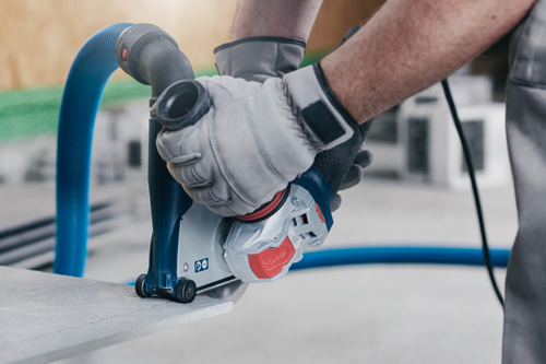 Bosch electric grinder being used by a person wearing gloves to cut a piece of stone, with a blue hose connected to it.