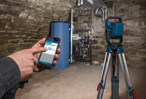 A hand using a smartphone to control the Floodlight. The phone displays the text 'Floodlight Control'. A Bosch floodlight is set on a tripod.