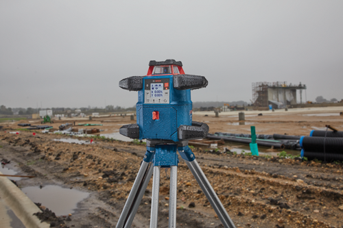 Bosch level tool, X 0.00%, Y 0.00% on a tripod at a construction site.
