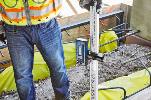 Person in blue jeans and a safety vest using a Bosch laser level.