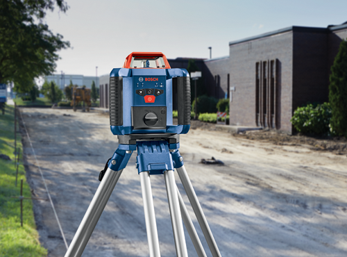 Bosch level, blue and red, set up on a tripod outdoors, "BOSCH" visible on the front