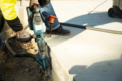 Bosch teal and black rotary hammer drill, with attached hose, breaking concrete.