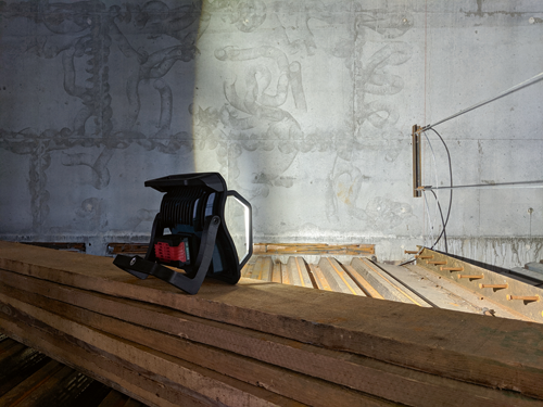 Black LED work light, stacked wooden beams, and a concrete wall with markings.