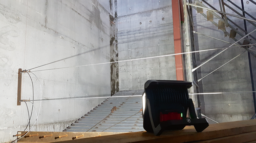 Large concrete wall with a metal staircase, cables, and a spotlight.